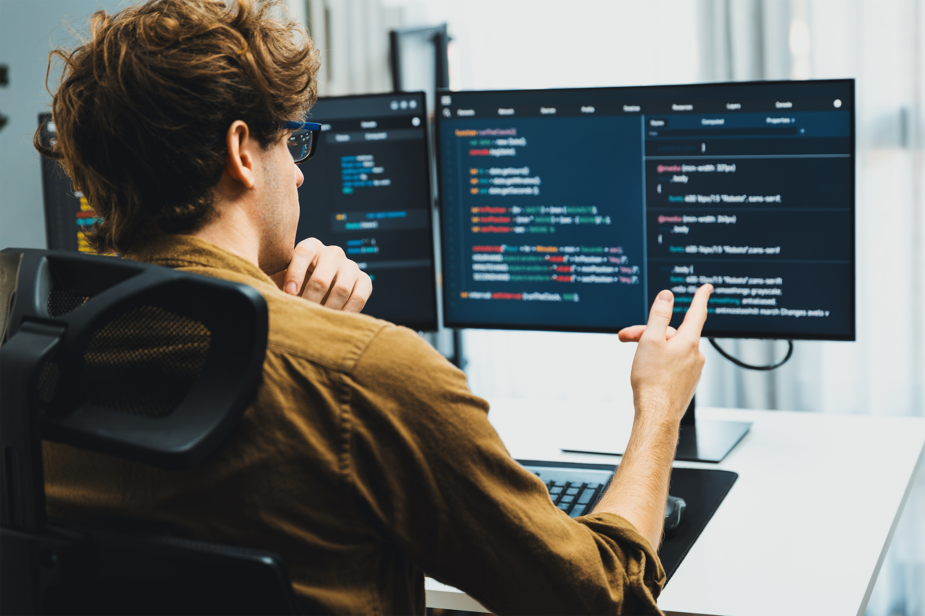 Eine Person, an einem Arbeitsplatz sitzend auf den 2 Bildschirmen ist Quellcode sichtbar.