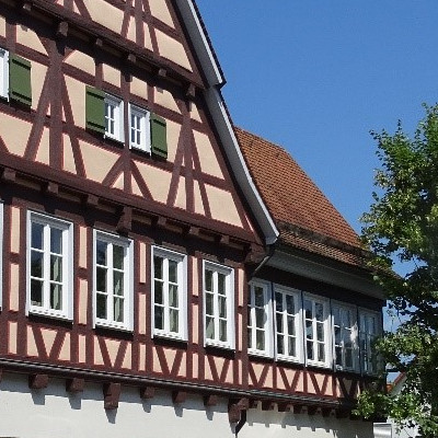 Fachwerkhaus in Urbach mit grünem Fensterladen und rotem Dach unter blauem Himmel.