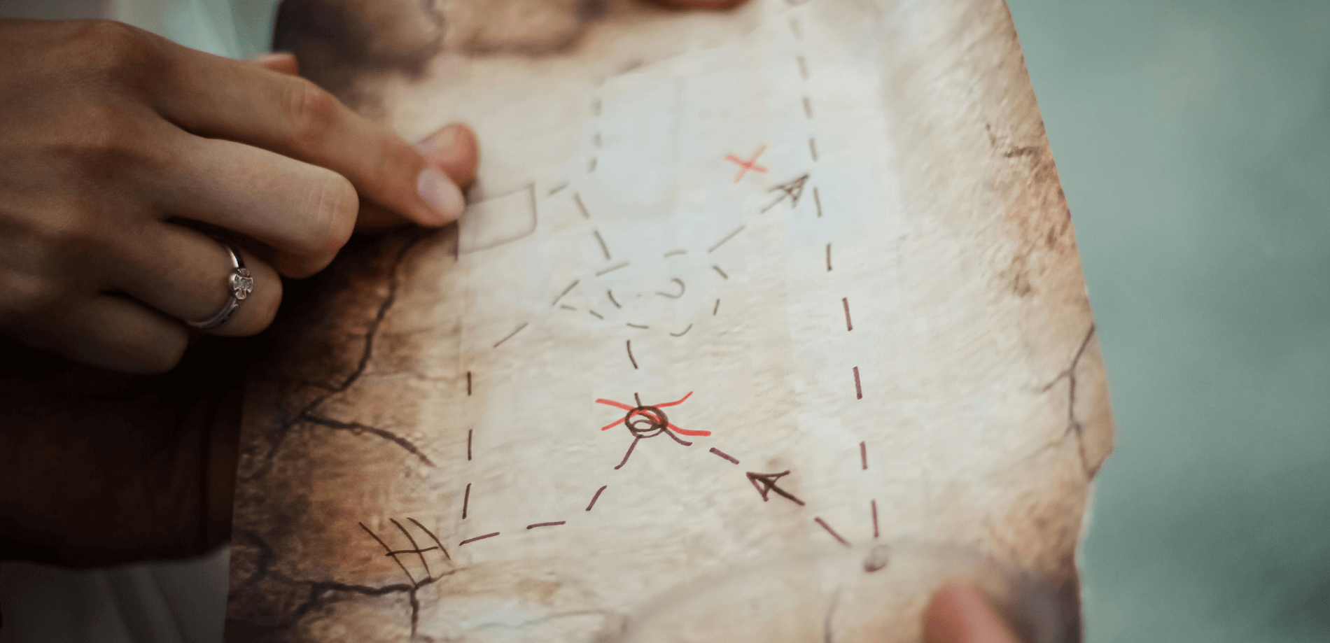 Eine Person hält eine alte Schatzkarte mit markierten Punkten und einer roten X-Markierung.