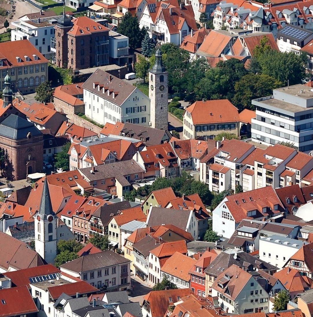 Luftaufnahme von Wiesloch mit roten Dächern, einer Kirche mit Turm und modernen Gebäuden im Hintergrund.