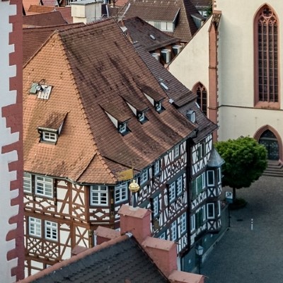 Blick auf historisches Fachwerkhaus mit rotem Dach und einer Kirche im Hintergrund.