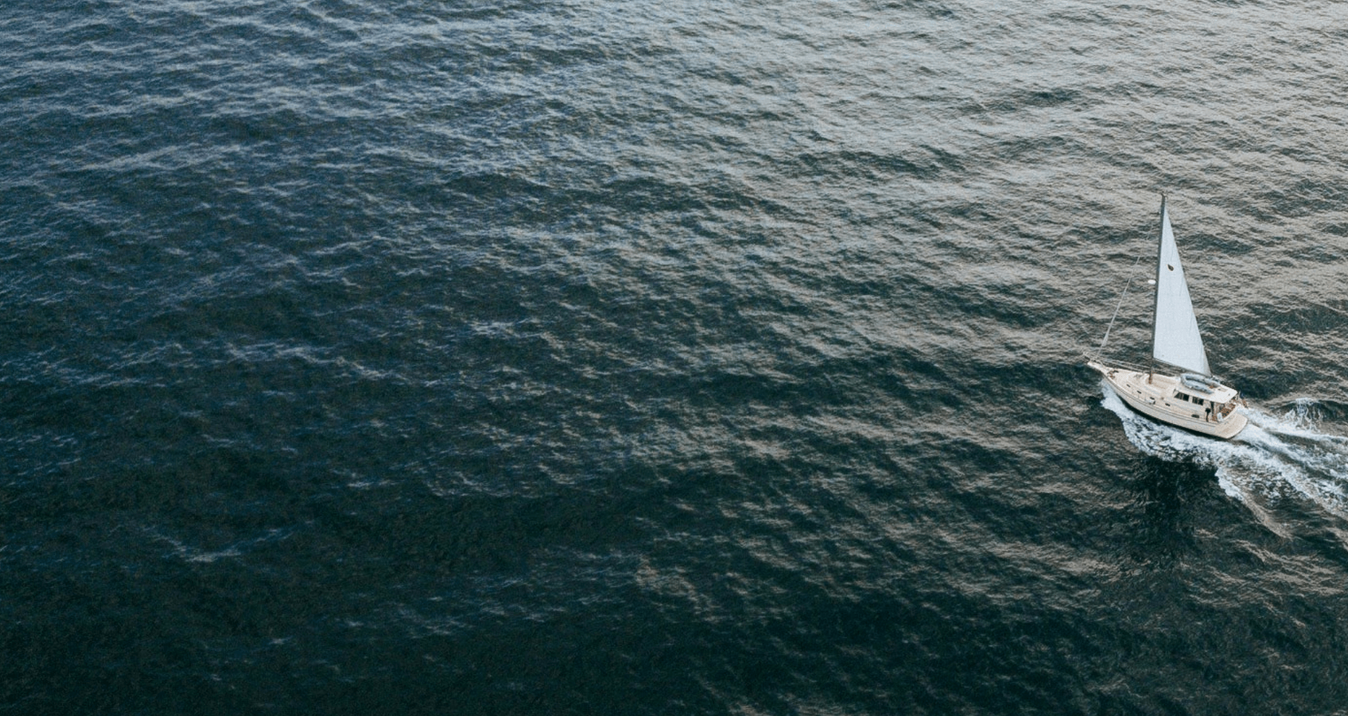 Ein Segelboot fährt über das offene Wasser, umgeben von tiefblauem Meer.