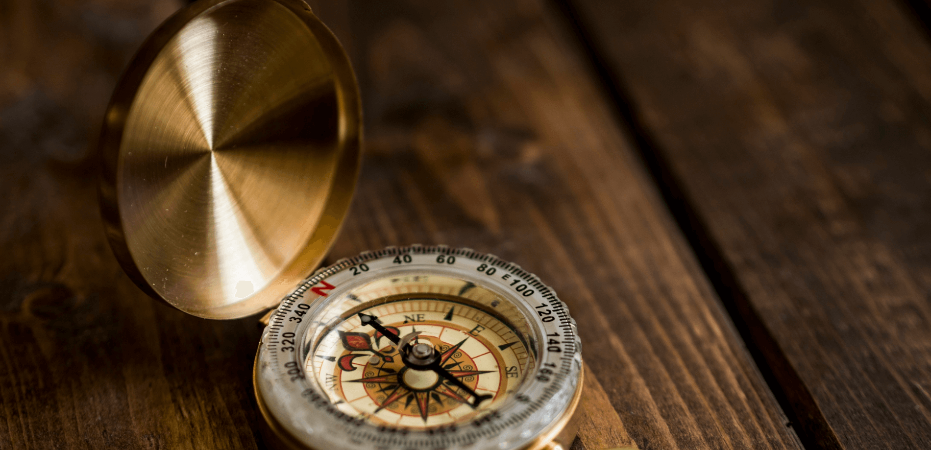 Eine offene Kompassnadel auf einem Holztisch, zeigt nach Norden mit klaren Ziffern und einem goldenen Gehäuse.