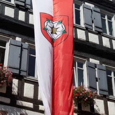 Eine rot-weiße Flagge mit dem Wappen von Rosenfeld vor einem Fachwerkgebäude.