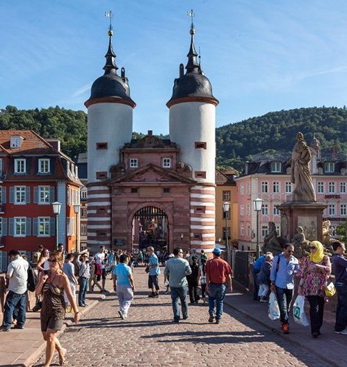 Das Heidelberger Tor mit zwei Türmen und einer Statue im Vordergrund, umgeben von Menschen und historischen Gebäuden.
