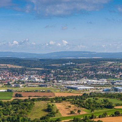 Luftaufnahme des Rhein-Neckar-Kreises. Eine Landschaft mit Feldern, Bäumen und einer Stadt mit Bergen im Hintergrund.