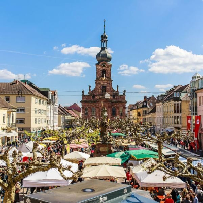 Großer Markplatz in Rastatt mit vielen Menschen und bunten Ständen. Im Hintergrund eine Kirche.