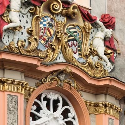 Detailansicht einer barocken Fassadengestaltung mit goldenen Verzierungen, Wappen und Figuren.