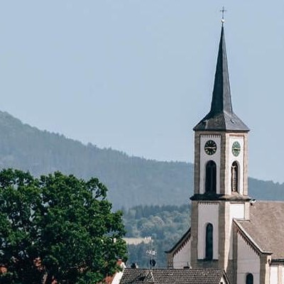 Kirchturm mit Uhr der Gemeinde Dauchingen mit einer Waldlandschaft im Hintergrund