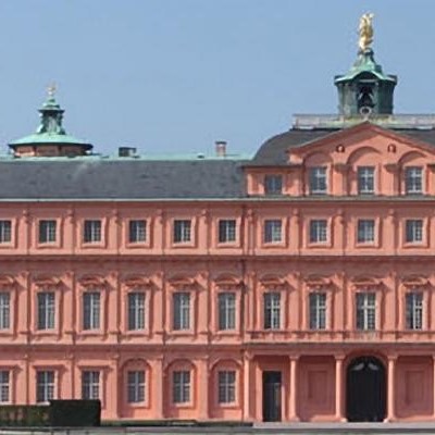 Das Barockschloss Mannheim mit rosa Fassade und goldener Statue auf dem Dach, umgeben von klarem Himmel.