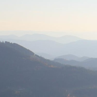 Sanfte, verschwommene Berglandschaft mit mehreren Hügeln und einer nebligen Atmosphäre im Hintergrund.